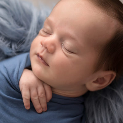 Newborn boy Aidan face close up and swaddled snuggly in blue wrap against blue fur in Gainesville FLorida