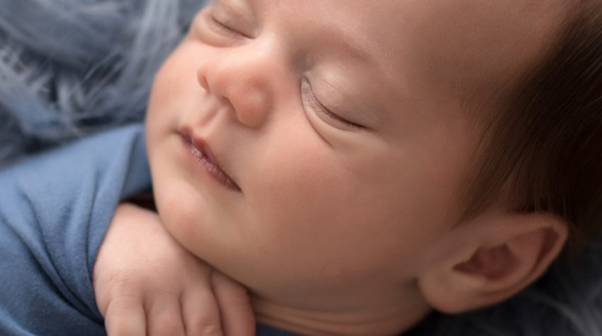 Newborn boy Aidan face close up and swaddled snuggly in blue wrap against blue fur in Gainesville FLorida