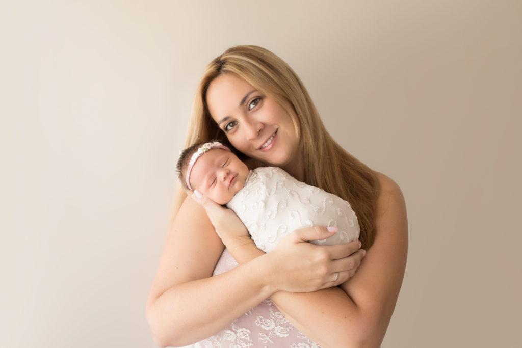Beautiful Mom in pink lace smiling and cuddling newborn girl wrapped in cream