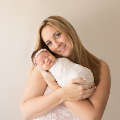 Beautiful Mom in pink lace smiling and cuddling newborn girl photos Gainesville FLoridawrapped in cream