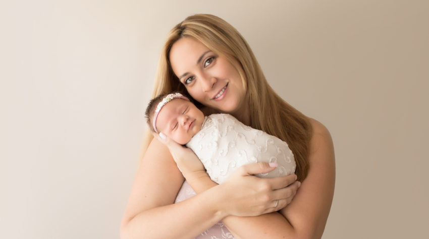 Beautiful Mom in pink lace smiling and cuddling newborn girl photos Gainesville FLoridawrapped in cream