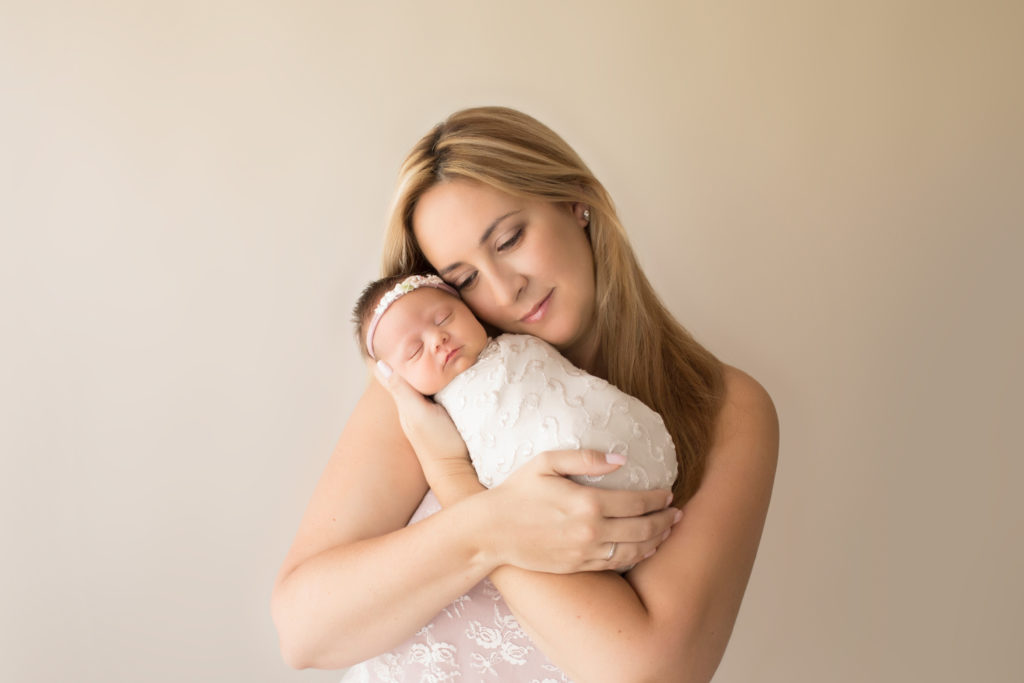 Beautiful Mom in pink lace cuddling newborn girl wrapped in cream