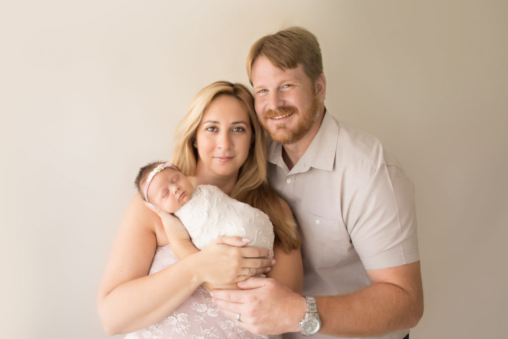 Beautiful Mom in pink lace and Dad in beige cuddling newborn girl wrapped in cream