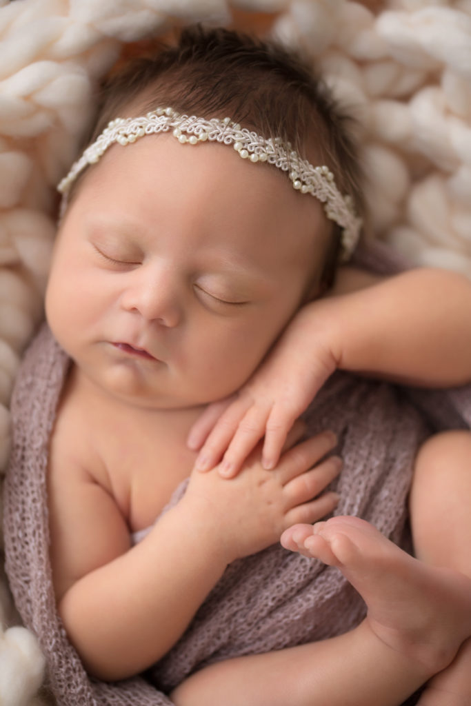 Newborn baby girl wrapped in pink close up face hands feet with pearl headband on head