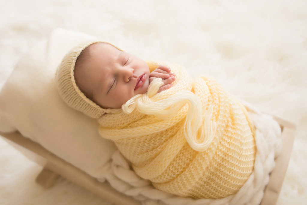 Newborn baby girl Bailey lying in cream bed wrapped in buttercream yellow knit blanket with matching bonnet Gainesville FL Andrea Sollenberger Photography