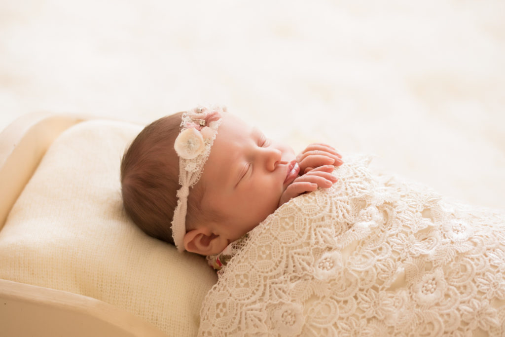 Newborn baby girl Bailey profile lying in cream bed wrapped in ivory lace with baby fingers wrapped on lace blanket lace headtie Gainesville FL Andrea Sollenberger Photography