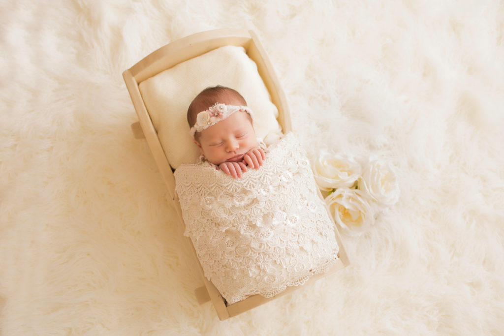 Newborn baby girl Bailey lying in cream bed wrapped in ivory lace with baby fingers wrapped on lace blanket and cream roses Gainesville FL Andrea Sollenberger Photography