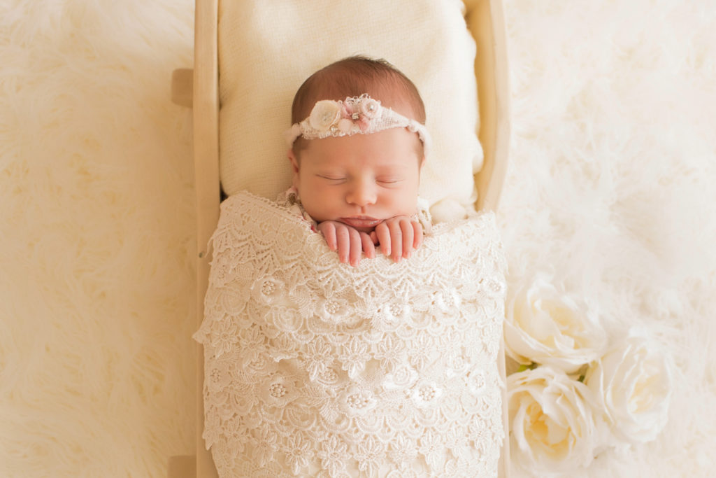 Newborn baby girl Bailey lying in cream bed wrapped in ivory lace with baby fingers wrapped on lace blanket and cream roses Gainesville FL Andrea Sollenberger Photography