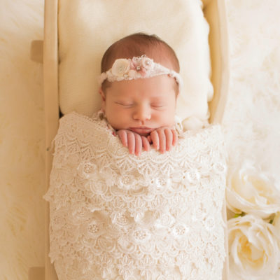 Newborn baby girl Bailey lying in cream bed wrapped in ivory lace with baby fingers wrapped on lace blanket and cream roses Gainesville FL Andrea Sollenberger Photography