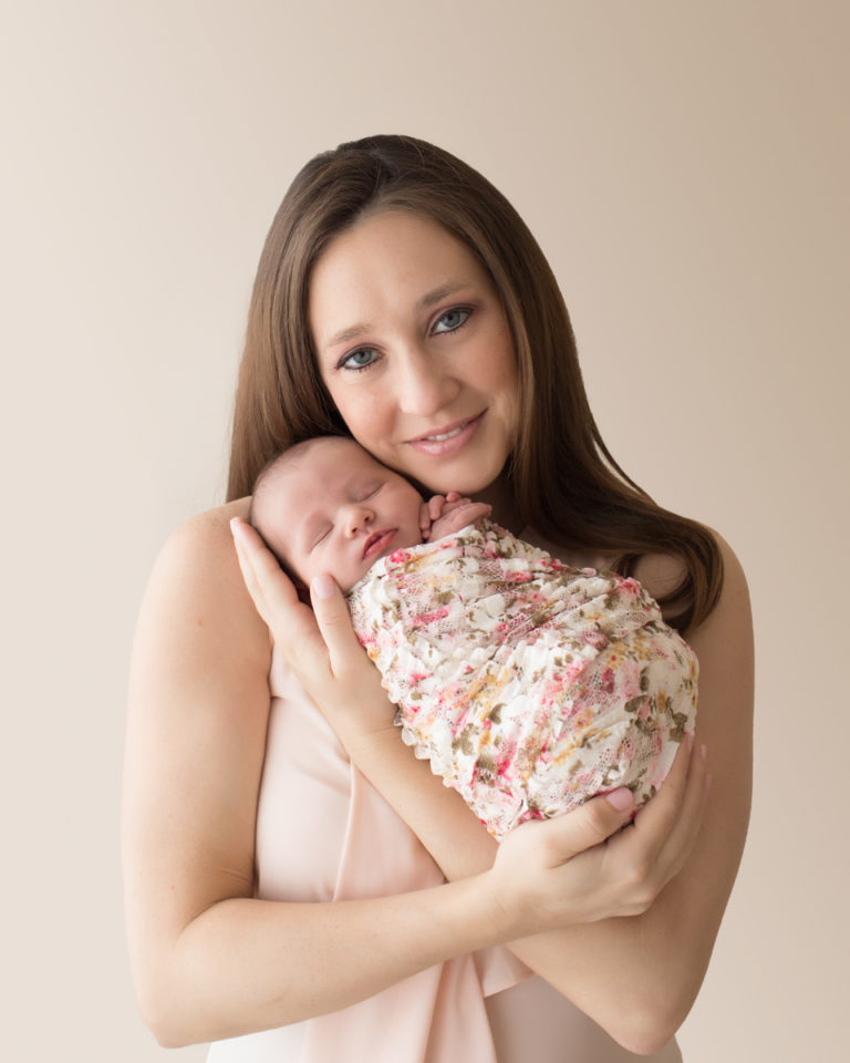 Gorgeous mom portrait smiling looking at camera cuddling newborn baby girl Bailey in pink floral wrap Gainesville FL Andrea Sollenberger Photography