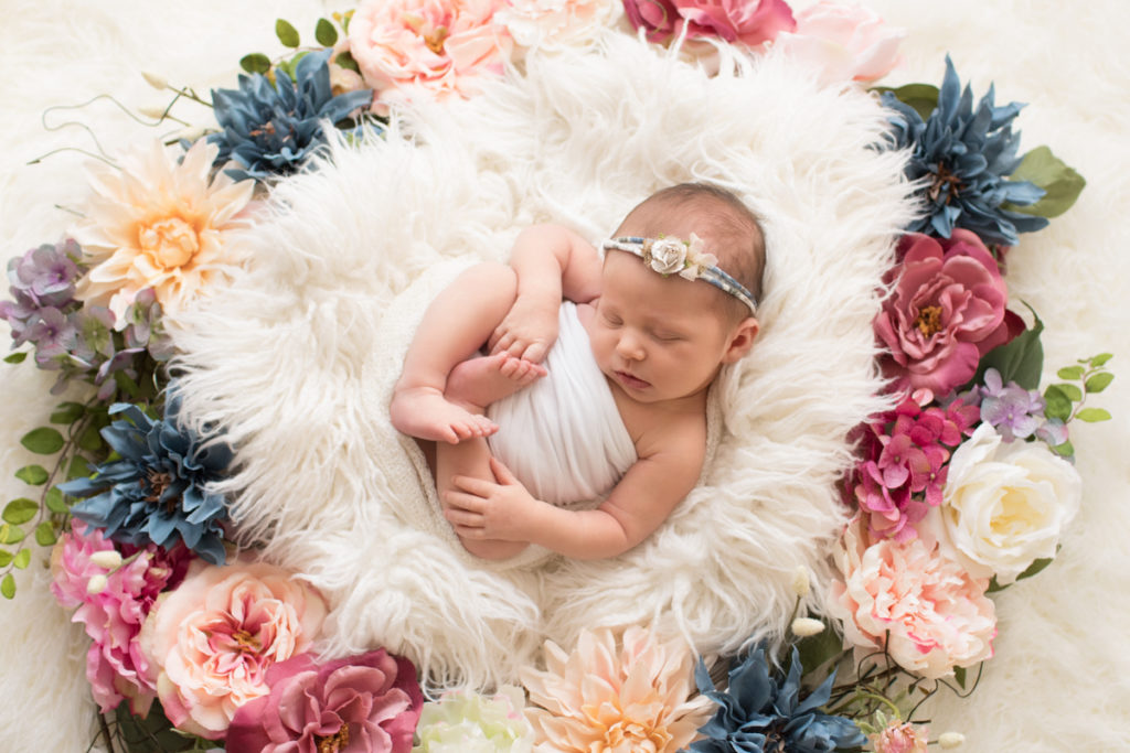 Newborn baby Bailey lying on back on white fur with floral headtie encircled with floral wreath Gainesville FL Andrea Sollenberger Photography