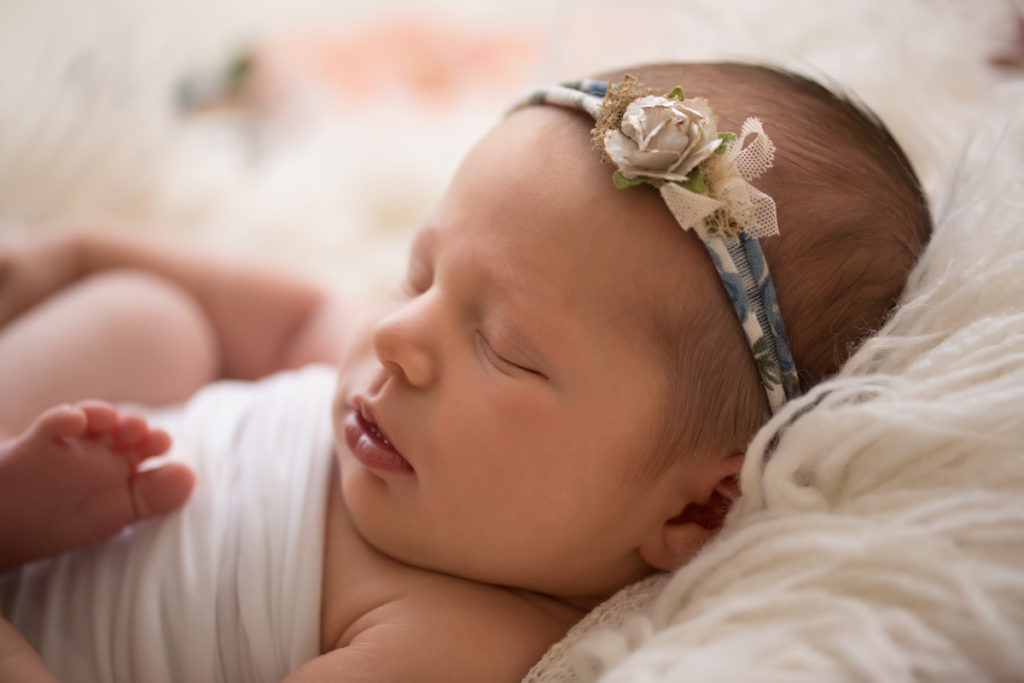 Newborn baby Bailey on white fur with floral headtie soft light Gainesville FL Andrea Sollenberger Photography