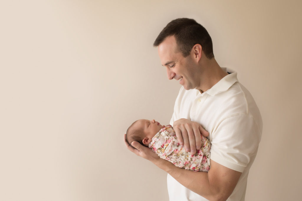 Handsome dad neutral color profile portrait smiling looking down and cuddling newborn baby girl Bailey in pink floral wrap Gainesville FL Andrea Sollenberger Photography