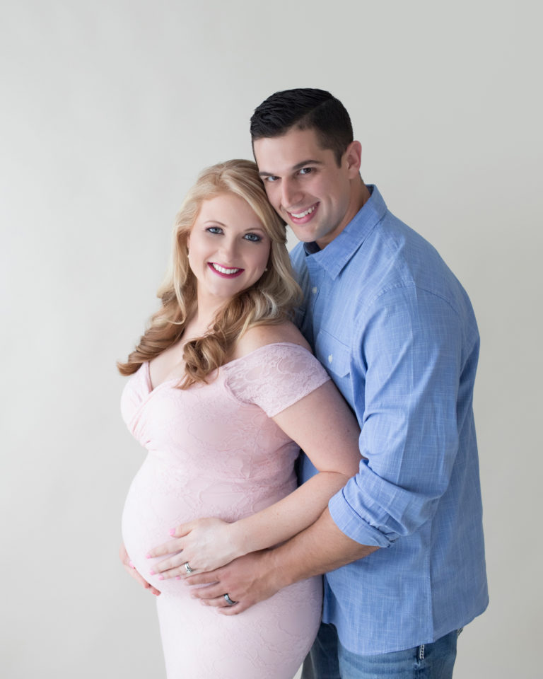 Maternity photos Christina with her man Jamie smiling his and hers hands holding beautiful belly bump wearing mermaid style full length pale pink lace gown Maternity Baby Photographer FL Gainesville