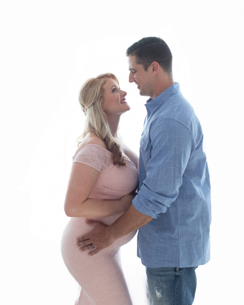 Maternity photos Christina mom face to face with husband Jamie against backlight looking down profile beautiful belly bump wearing mermaid style full length pale pink lace gown Gainesville Florida