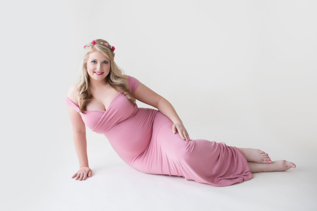 Maternity photos Christina posed on floor smiling at camera wearing mermaid style full length rose pink gown with floral crown Gainesville Florida