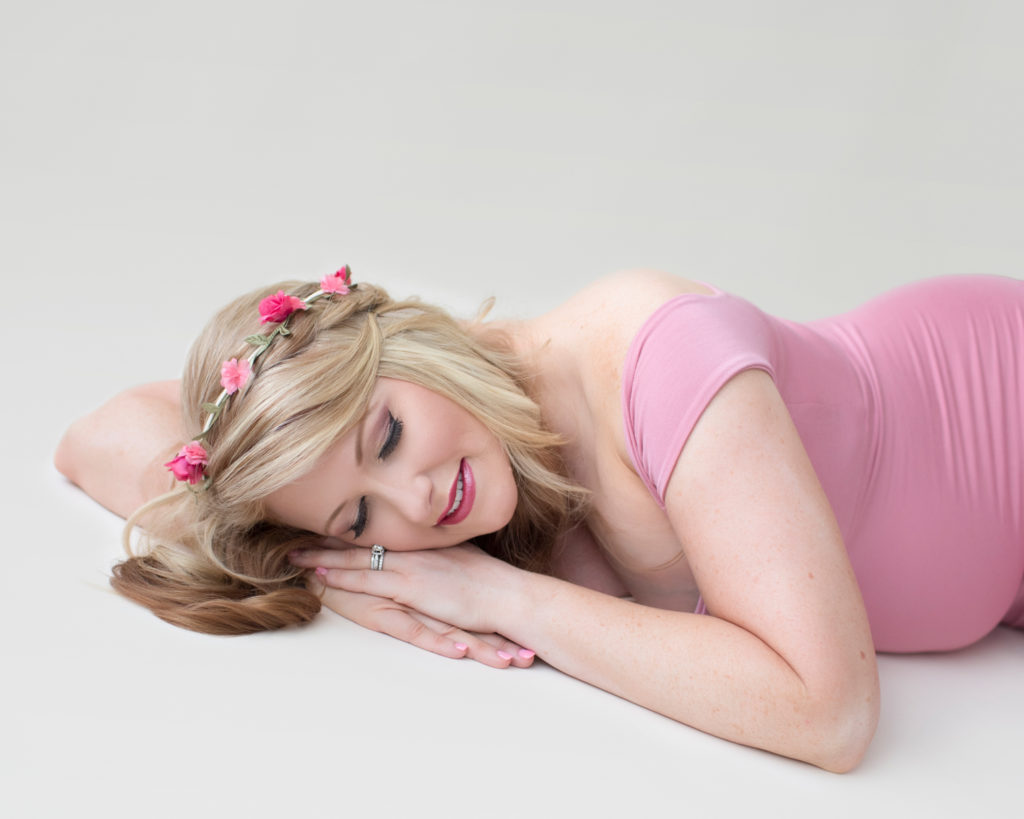 Maternity photos Christina eyes cloed and smiling wearing mermaid style rose pink gown posed on floor with floral crown Gainesville Florida