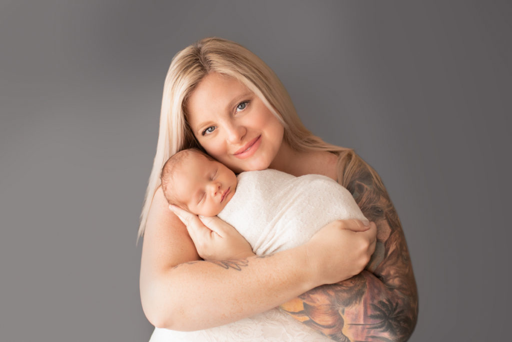 Mom with arm tatoo looking up smiling and cuddling newborn baby Rowan Gainesvile Florida Photos