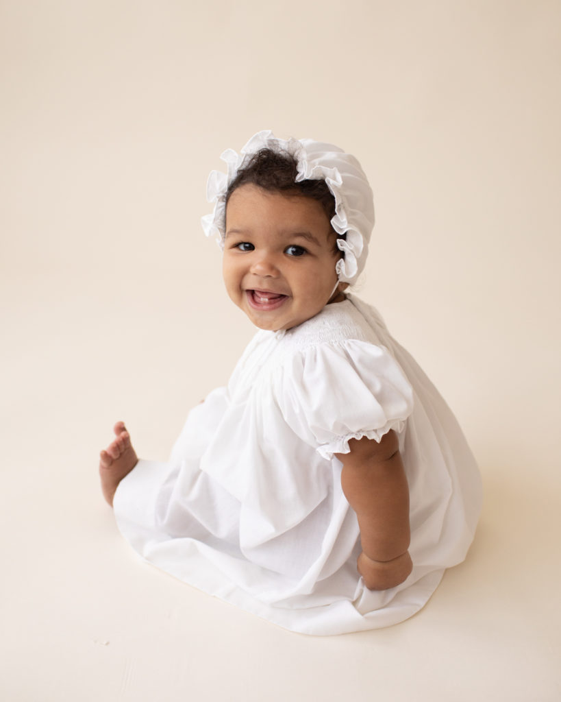 Baby 6 months old smiling sitting up in white cotton dress and matching bonnet Gainesville FL