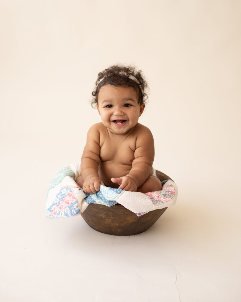 Baby 6 months old smiling sitting in wood bowl with quilt in Gainesville FL
