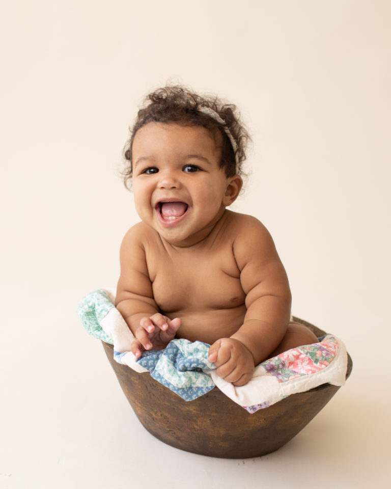 Baby 6 months old smiling with mouth open sitting in wood bowl with quilt in Gainesville FL