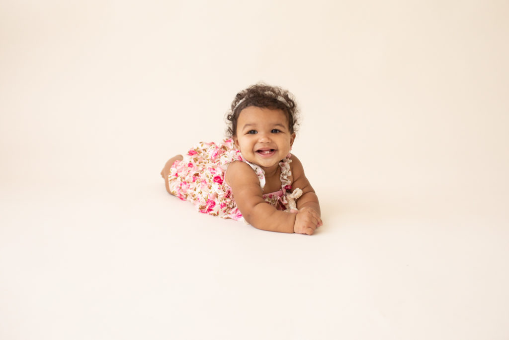 Baby 6 months old smiling pushing up on white floor dressed in pink floral jumper in Gainesville FL