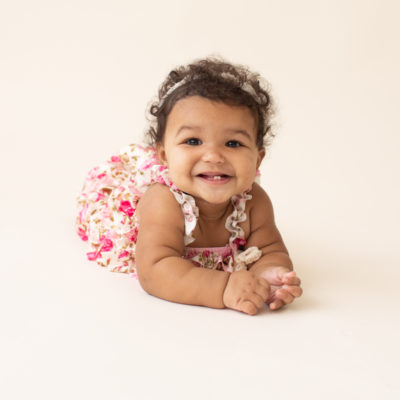 Baby 6 months old smiling pushing up on elbows on white floor dressed in pink floral jumper in Gainesville FL