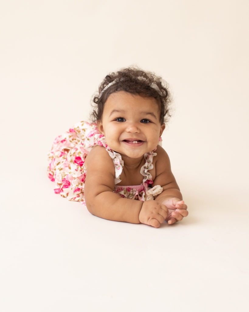 Baby 6 months old smiling pushing up on elbows on white floor dressed in pink floral jumper in Gainesville FL