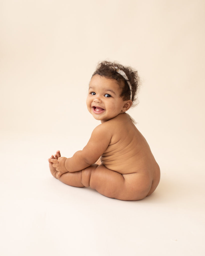 Milestone session 6 months old smiling naked with soft squishy baby rolls on white floor in Gainesville FL