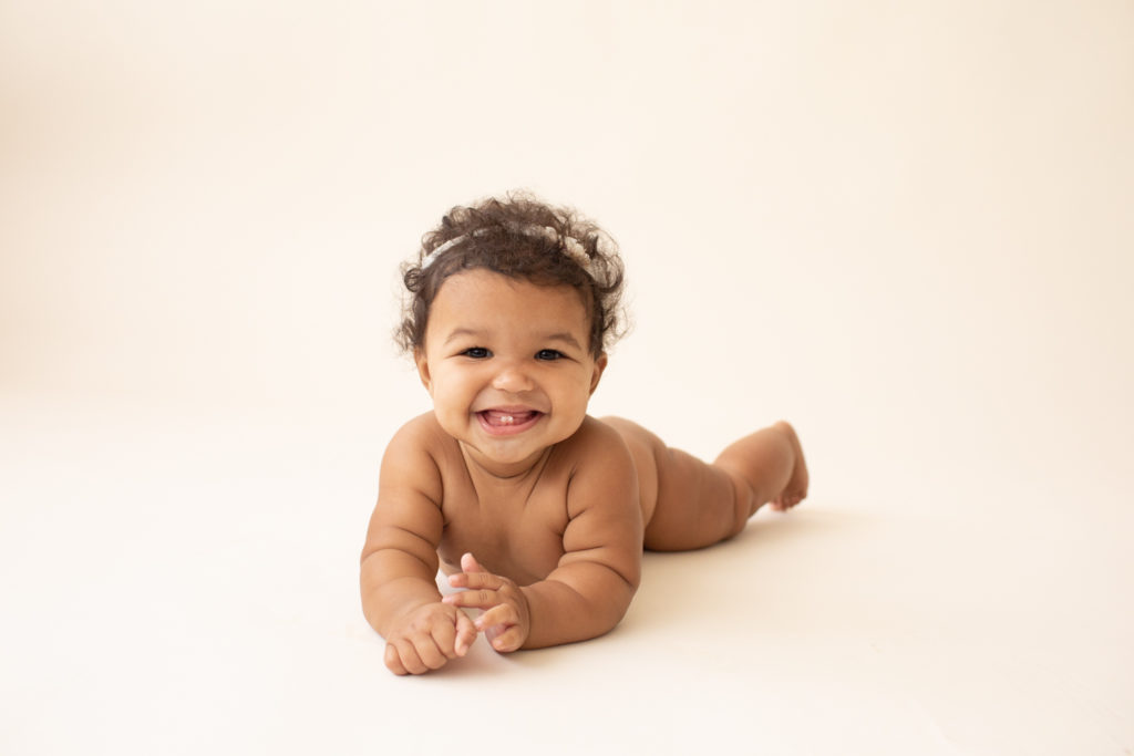 Milestone session 6 months old smiling naked with soft squishy baby rolls lying on belly pushing up to elbows on white floor in Gainesville FL