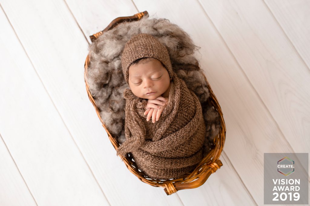 Award winning newborn photography baby wrapped in bown knit bundle lying in basket with brown fur