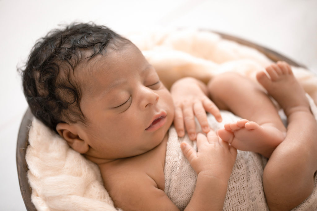 Newborn Jacob photos close up with full head of hair wrapped in cream knit wrap on cream fur in brown wood bowl against cream wood floor Gainesville FL