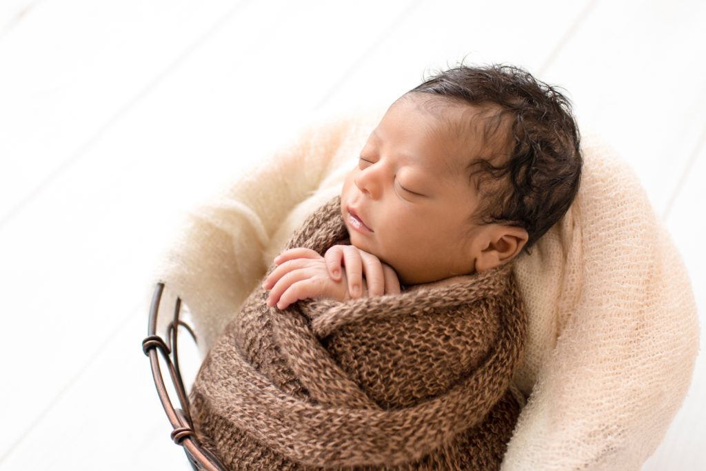 Newborn Jacob photos with full head of hair profile wrapped in knit brown wrap potato sack in metal basket against cream wood floor Gainesville FL