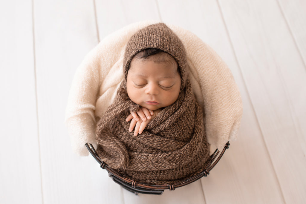 Newborn Jacob photos with full head of hair wrapped in knit brown wrap potato sack in metal basket against cream wood floor Gainesville FL