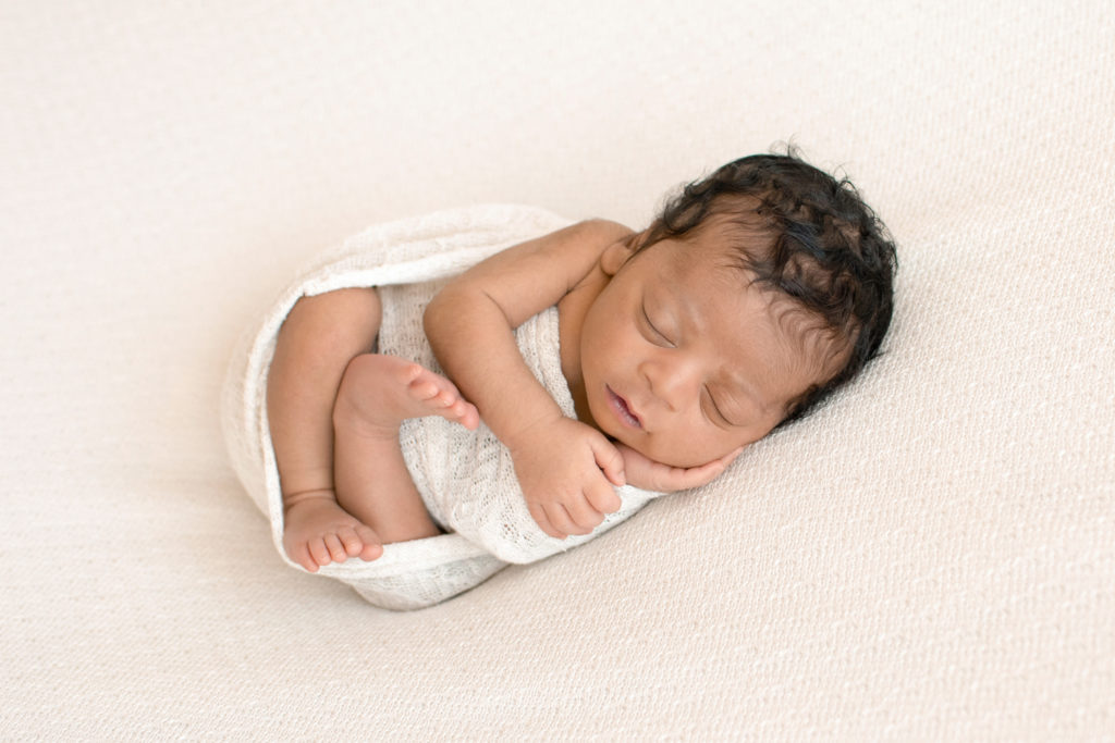 Newborn Jacob photos with full head of hair wrapped in cream knit wrap posed on cream blanket Gainesville FL
