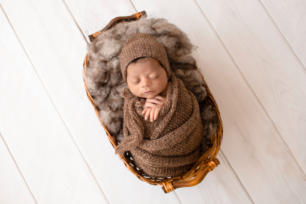 Newborn Jacob photos with full head of hair wrapped in knit brown wrap potato sack on brown fur in basket Gainesville FL