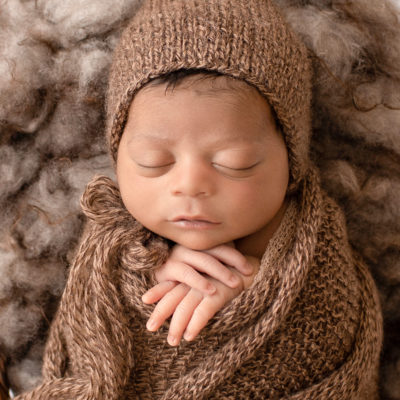 newborn pictures Jacob face close up with full head of hair wrapped in knit brown wrap potato sack on fur stuffed brown basket Gainesville FL