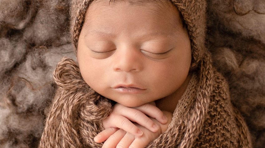 newborn pictures Jacob face close up with full head of hair wrapped in knit brown wrap potato sack on fur stuffed brown basket Gainesville FL