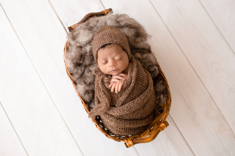 newborn pictures Jacob with full head of hair wrapped in knit brown wrap potato sack on fur stuffed brown basket Gainesville FL