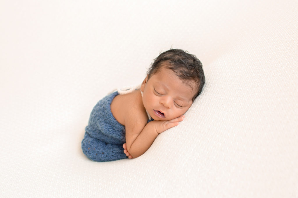 Newborn Jacob photos in blue knit overalls with full head of hair posed on cream blanket Gainesville FL