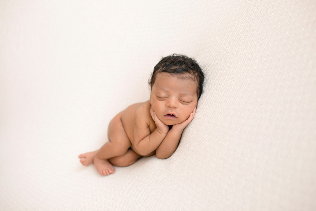 Newborn Jacob photos with full head of hair posed naked with face cupped in his own hands on cream blanket Gainesville FL