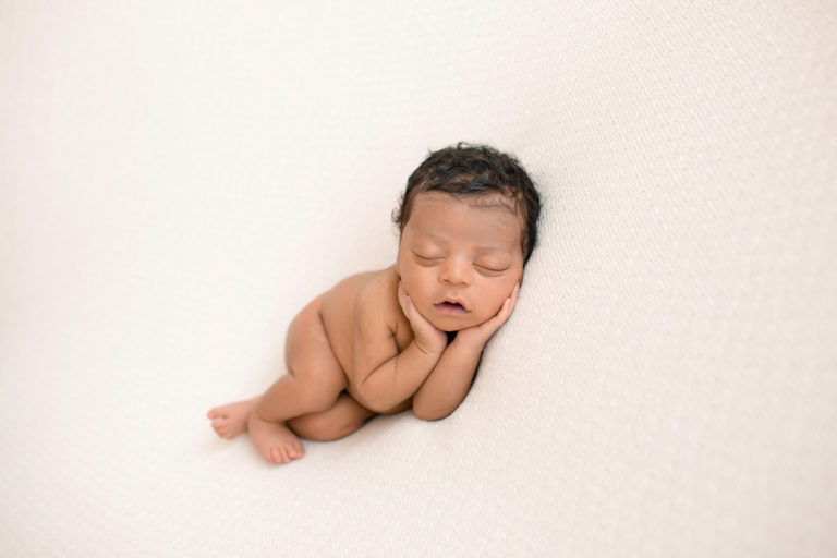 newborn pictures Jacob with full head of hair posed naked with face cupped in his own hands on cream blanket Gainesville FL