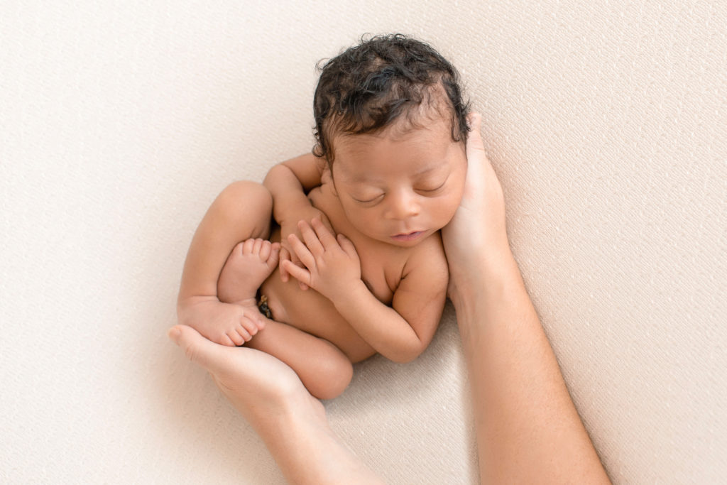 Newborn Jacob photos with full head of hair posed naked in moms hands on cream blanket Gainesville FL
