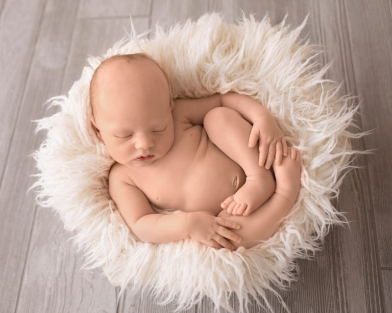 Gainesville Newborn Boy Gavin naked in white fur stuffed bowl on grey wood floor tiny baby details hands feet soft baby skin Andrea Sollenberger Photography