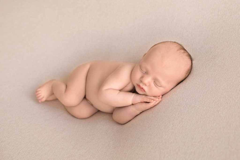 Gainesville Newborn Boy Gavin naked pose on beige blanket lying on side with newborn hands cupping face Andrea Sollenberger Photography