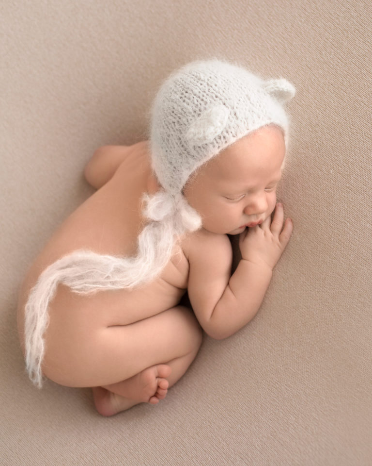 Gainesville Newborn Boy Gavin naked pose on beige blanket with bottom up and white knitted bear bonnet looking down Andrea Sollenberger Photography