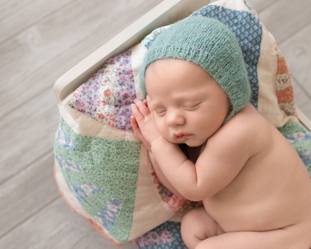 Gainesville Newborn Boy Gavin close up posed on quilt covered white bed with teal knit bonnet tiny baby details hands soft baby skin Andrea Sollenberger Photography
