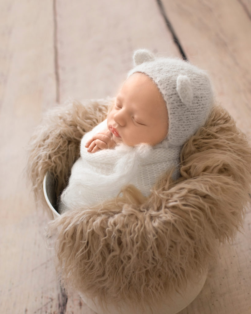 Gainesville Newborn Boy Gavin white knitted wrap potato sack and white knitted bear bonnet in white bucket stuffed with beige fur profile shot Andrea Sollenberger Photography