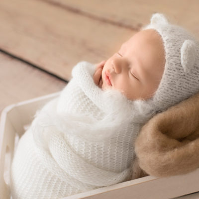 Gainesville Newborn Boy Gavin profile photo potato sack white knit wrap and bear hat on beige blanket in white crate