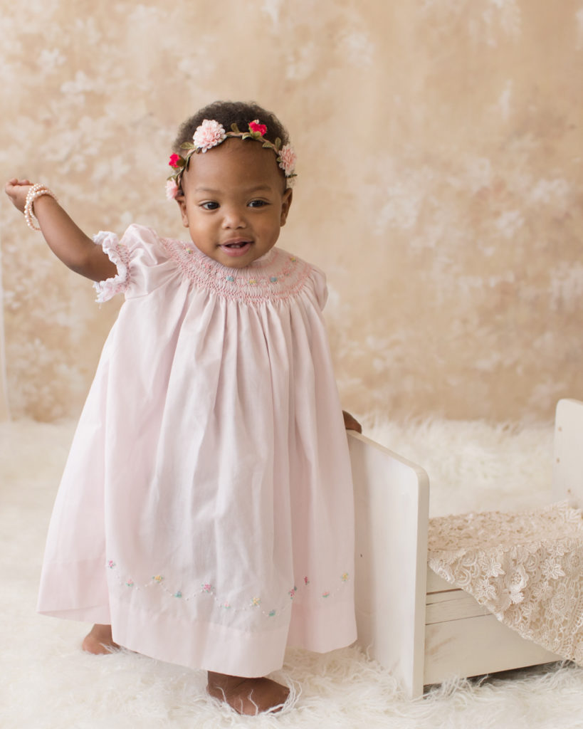 Rose One Year Old Baby Photos standing with pink smocked dress and floral crown pearls and ivory lace Gainesville Florida